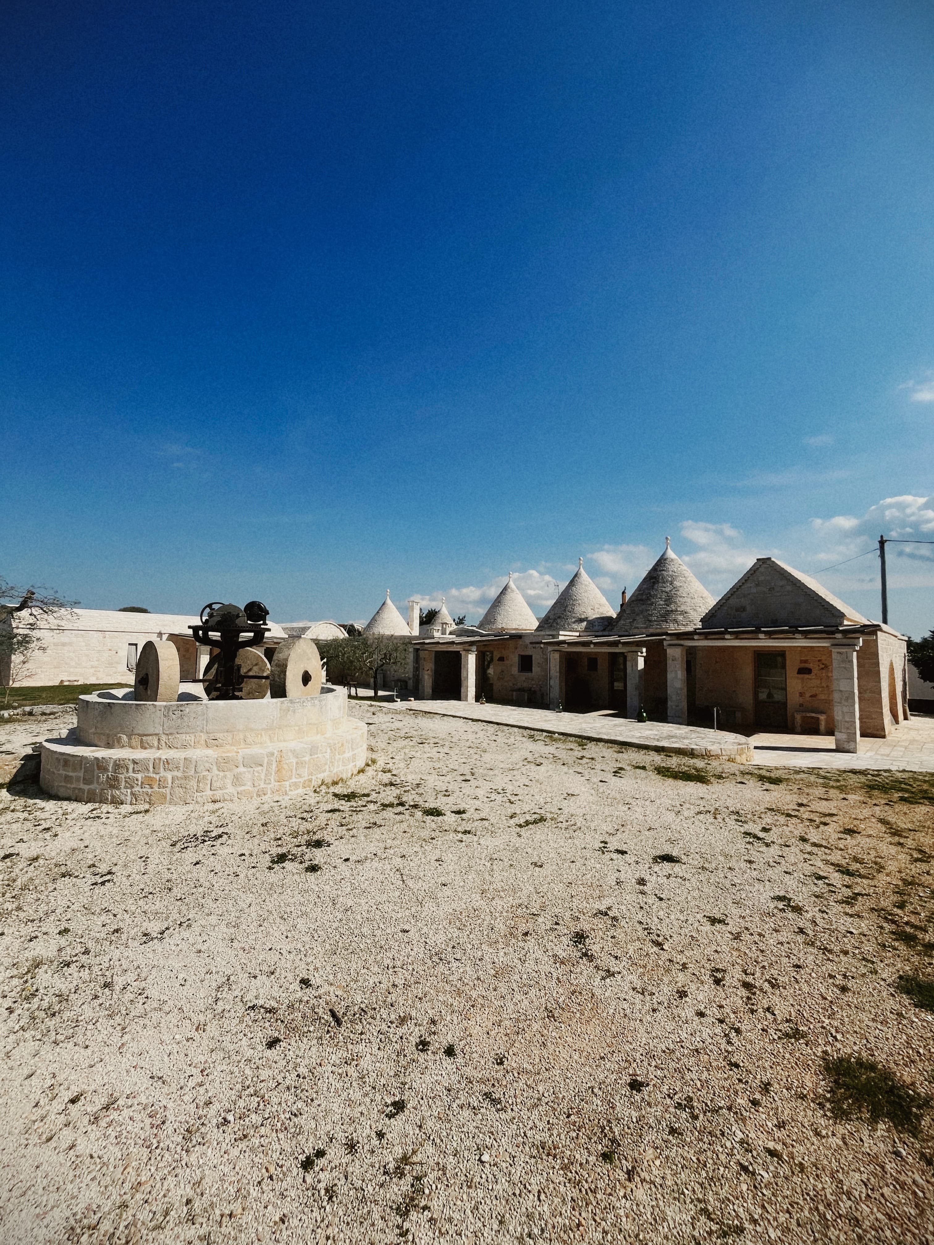 Corte dei trulli con macina in pietra, cielo azzurro